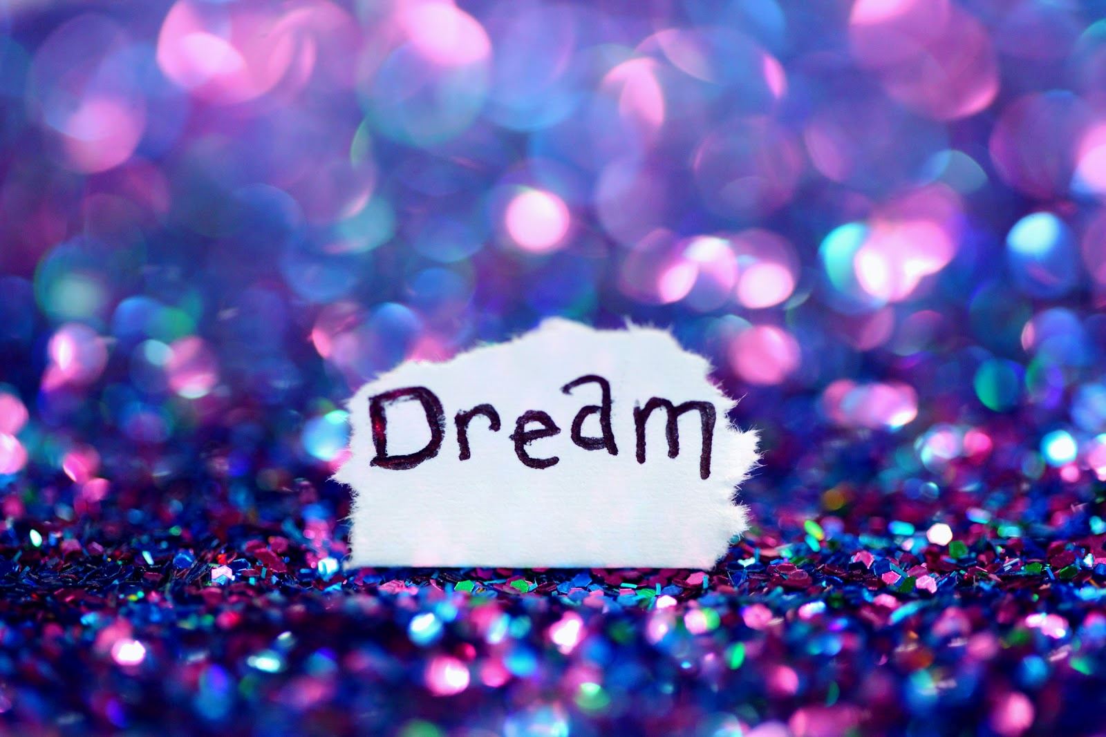 Word ‘Dream’ on white splash, on background of purple and pink glitter